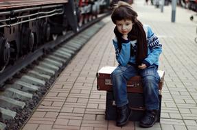 European child Boy Sitting on Suitcase at train on railway