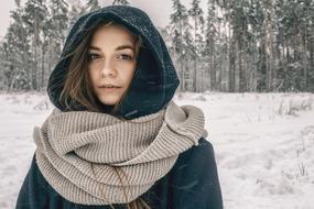 Portrait of the girl in warm clothes among the plants in snow in winter