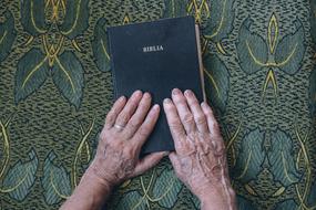 two hands of an elderly man on the bible