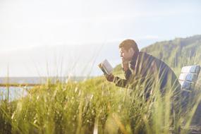 young Man reading book on bench in wilderness