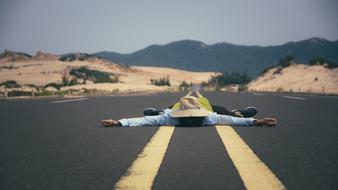 Man with wide open hands lays on asphalt road in wilderness