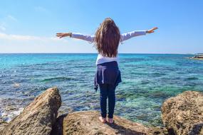 girl with raised hands on a stone by the sea