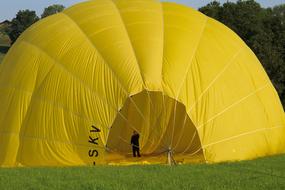 Man, in the yellow gas tight envelope balloon, with the black sign, on the green meadow, near the trees