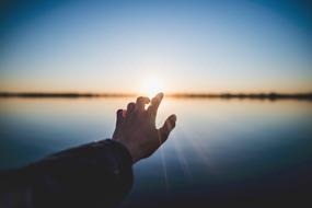 hand pointing to sun at horizon above water