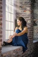 Woman in blue dress sitting on the windowsill of the brick building