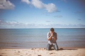 despair, man kneels down on beach at sea