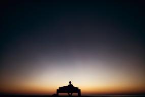 optical photo of a lone person on a bench against a sunset background