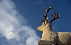 Profile portrait of the beautiful deer statue with antlers at blue sky with white clouds