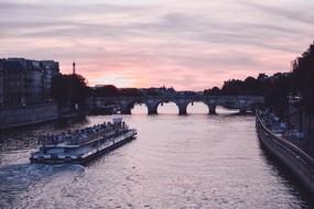 Boat on the water, among the buildings, on the beautiful Paris cityscape, at colorful sunset, in France