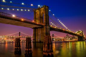 colorful illuminated Brooklyn Bridge above river at night, usa, nyc