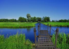 wooden pier on the river against the background of a green field at sunrise