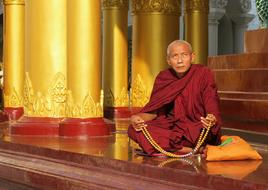 old buddhist monk in red clothing prays with rosary beads in temple