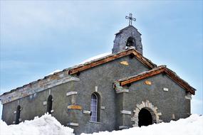 Beautiful chapel with the cross, among the white snow, under the blue sky with white clouds, in winter