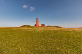 lighthouse with orange walls on a green hill