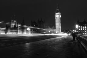 Black and white photo of the beautiful London with the Big Ben clock on the tower, Parliament, and lights in motion, on the Bridge, in England, United Kingdom