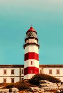 Beautiful, red and white lighthouse on the shore, near the building in Spain