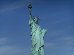 Green Statue of Liberty at blue sky background with white clouds