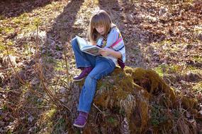 girl reading a book in the shade among nature