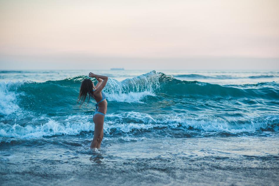 girl in bikini in waves in bali at dusk