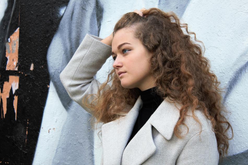 Portrait of the beautiful girl with curly hair, in white coat
