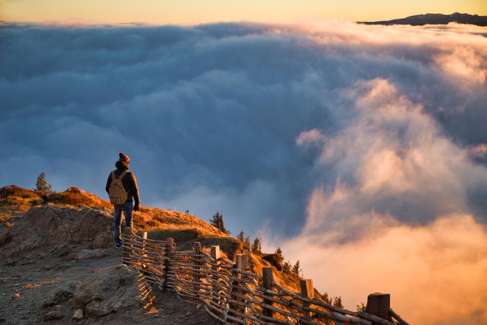 hiker on the mountain summit and clouds below
