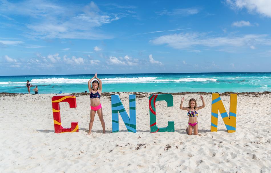 girls in swimsuits near the sign on the beach