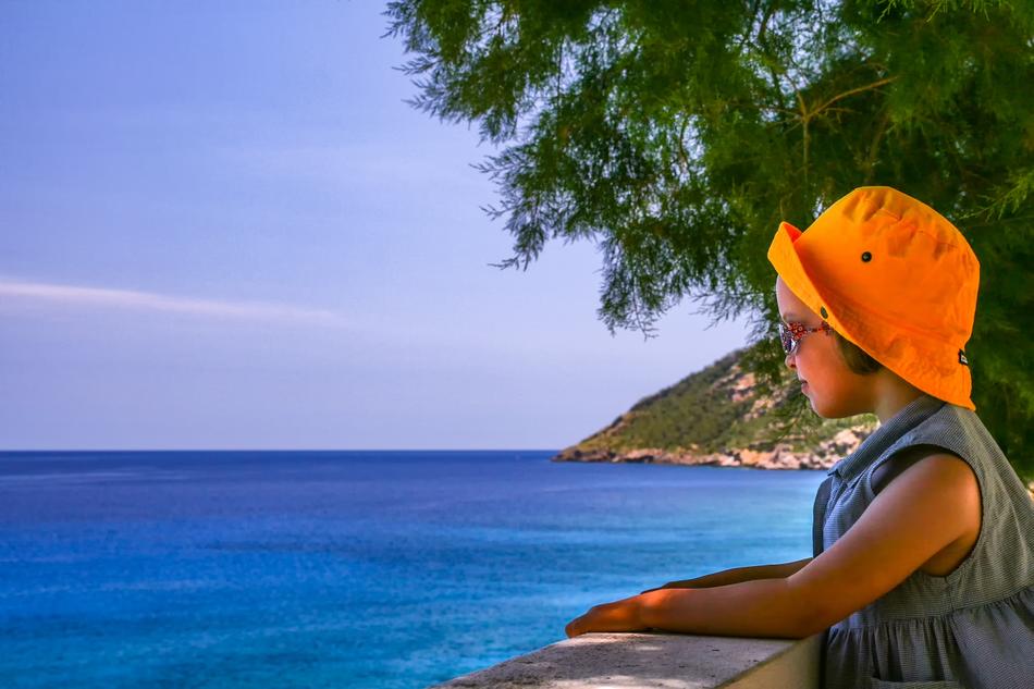 girl in orange panama looks at the sea