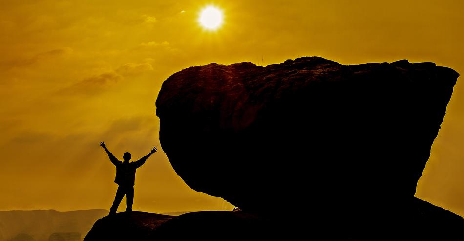 silhouette of man with raised hands on cliff at golden sunset