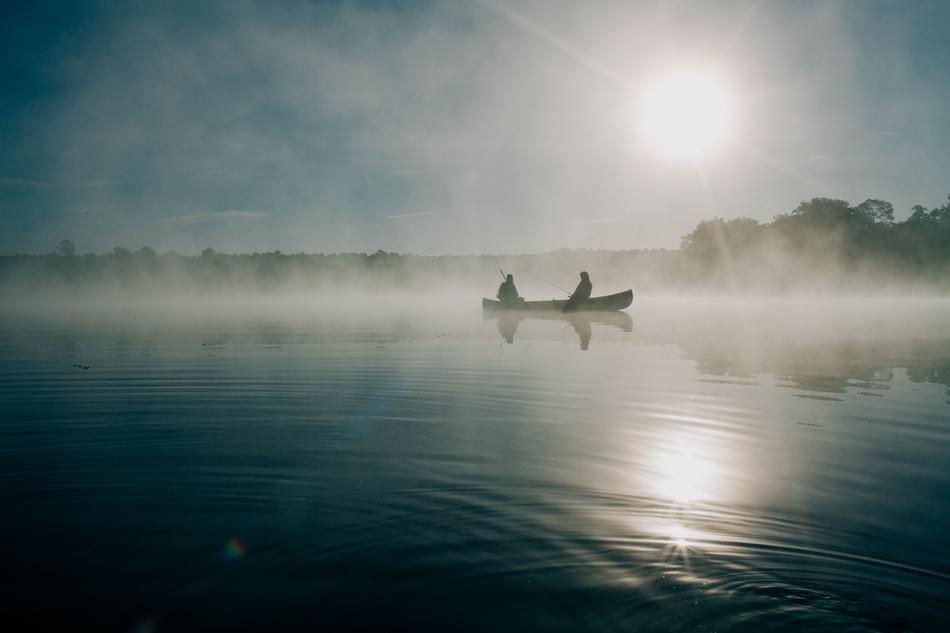 People, fishing on the boat, on the beautiful, foggy lake, in light, among the trees