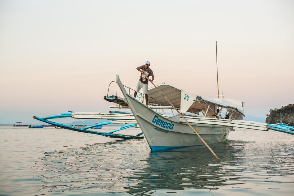 Man, near the blue and white boat in the port of Puerto Galera, Mindoro, Philippines, at colorful and beautiful sunset