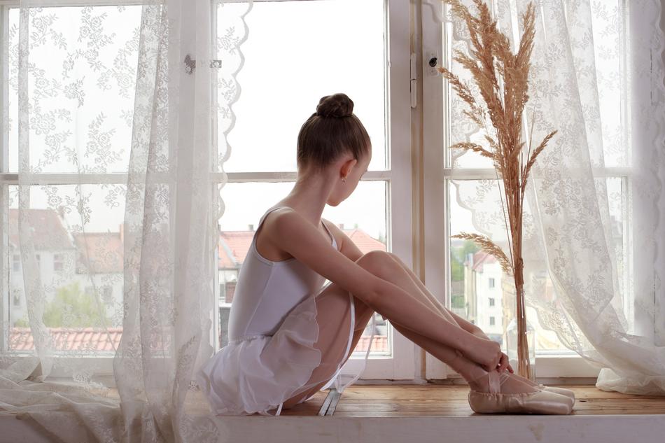 Ballerina in beautiful white dress and shoes, sitting near the white window