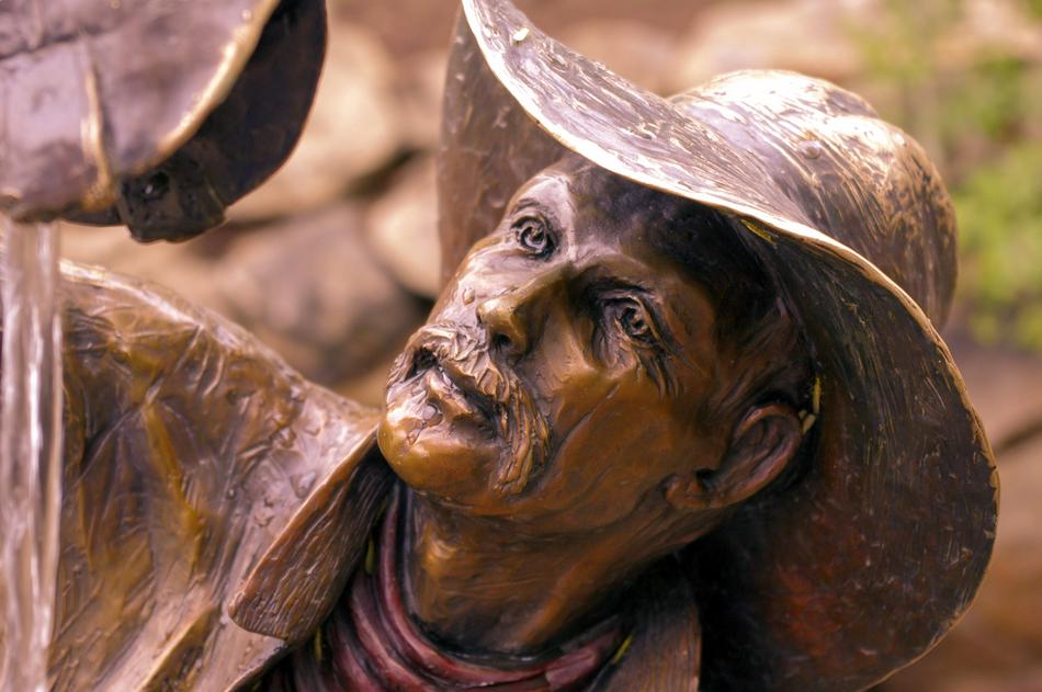 Shiny, bronze sculpture of the Wishful Thinkin Cowboy, in the park of Colorado, in light