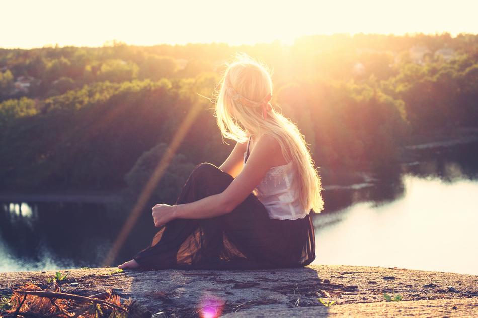 blonde sitting on a stone by the lake against the background of dawn
