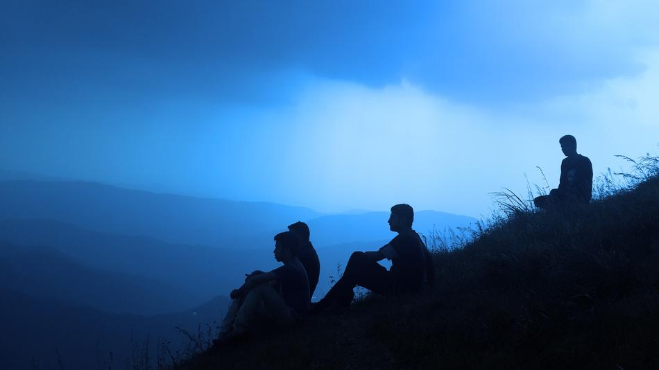 Silhouettes of four Men sitting on hill side at dusk