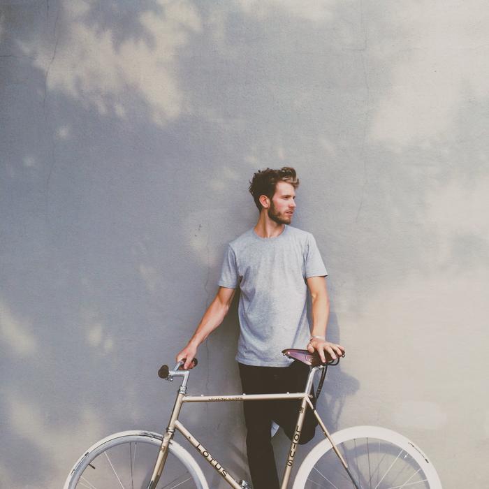 Bearded man, posing with the bike, near the water with the tree shade, in light