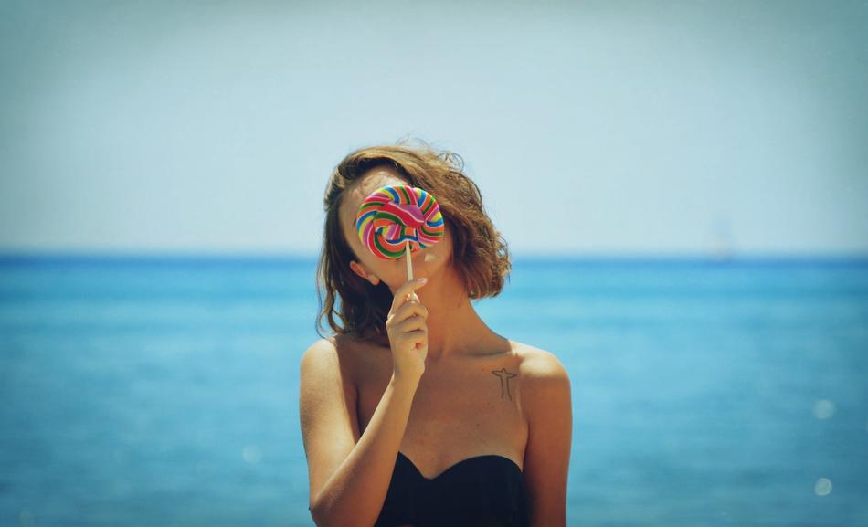 young girl holds colorful candy at face in front of Sea