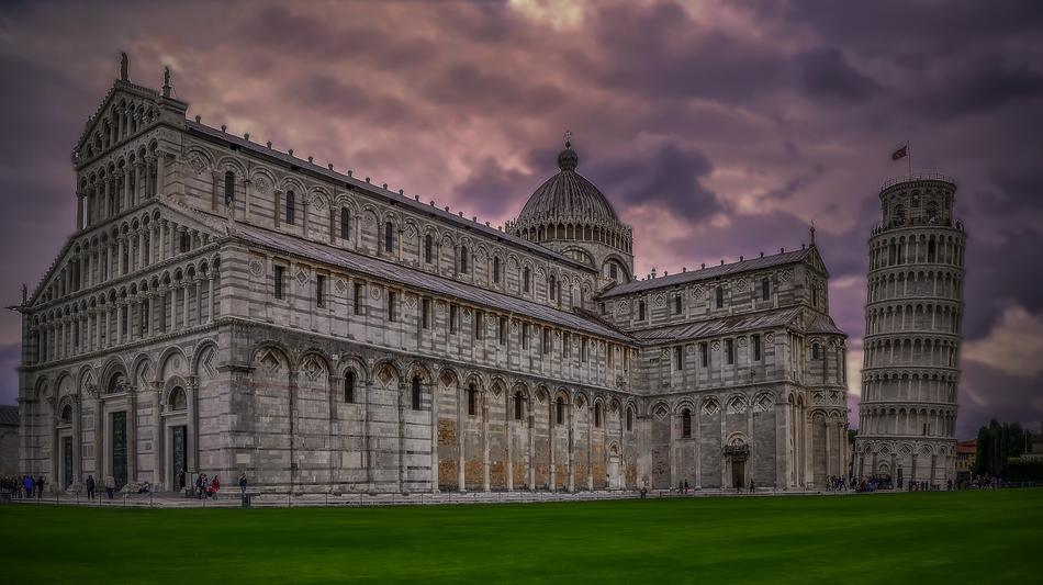 Beautiful Leaning Tower of Pisa and castle on the green field, at colorful sunset in the sky, in Pisa, Italy