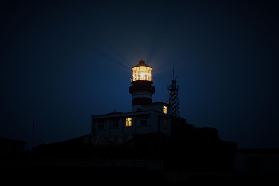 lighthouse with bright light on a hill in the dark