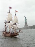 photo of a sailing ship on the background of the Statue of Liberty