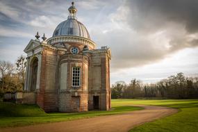 Beautiful building with the dome, among the green fields and trees, under the blue sky with clouds
