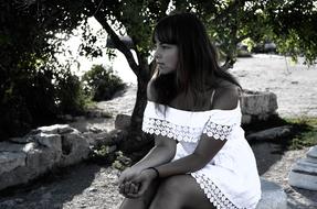 Girl in white dress, sitting on the rocks, near the green plants, in Hersonissos, Greece