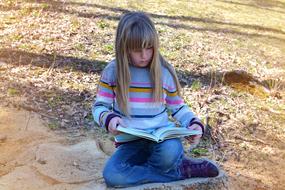 blonde girl reading a book in nature