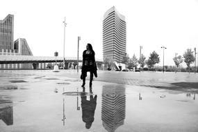 black and white, girl is reflected in a puddle against the background of city buildings