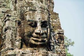 Beautiful stone face of Angkor Wat among the green trees in Cambodia