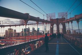 Silhouette of the person, on the colorful suspension bridge, near the buildings, under the blue sky with clouds