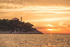 Beautiful, green, rocky shore with the house and lighthouse on the shore at colorful sunset in Croatia