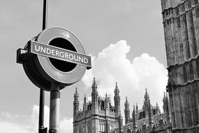 Black and white photo with the "Underground" sign, near the beautiful building in London, England, UK