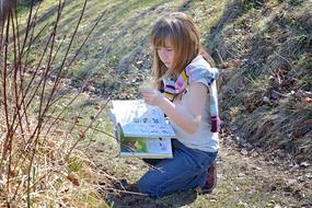 Child girl, reading a book on the beautiful landscape with green grass