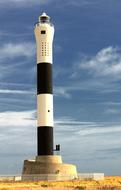 White and black lighthouse on the Dungeness coast in England, under the blue sky with white clouds