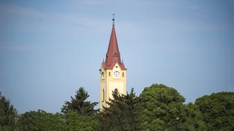 Beautiful church steeple, behind the green trees, at blue sky with clouds on background